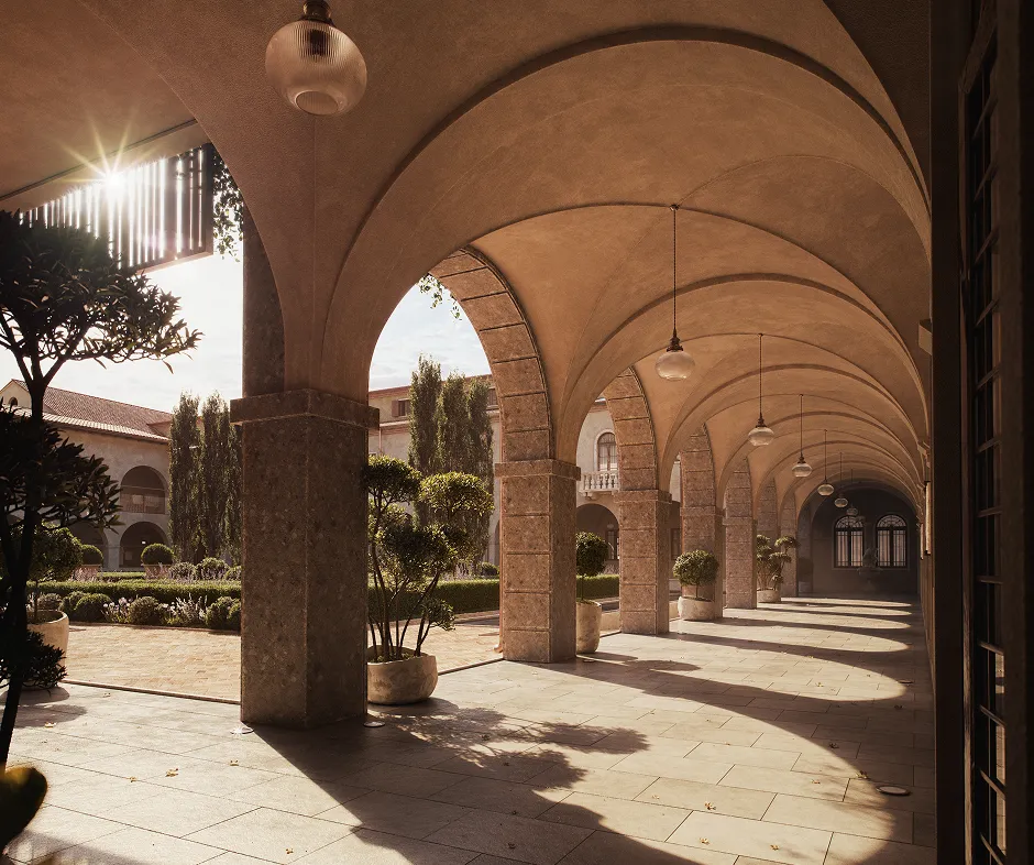 Arched stone corridor with hanging lamps and potted plants, sunlight casting shadows on tiled floor.
