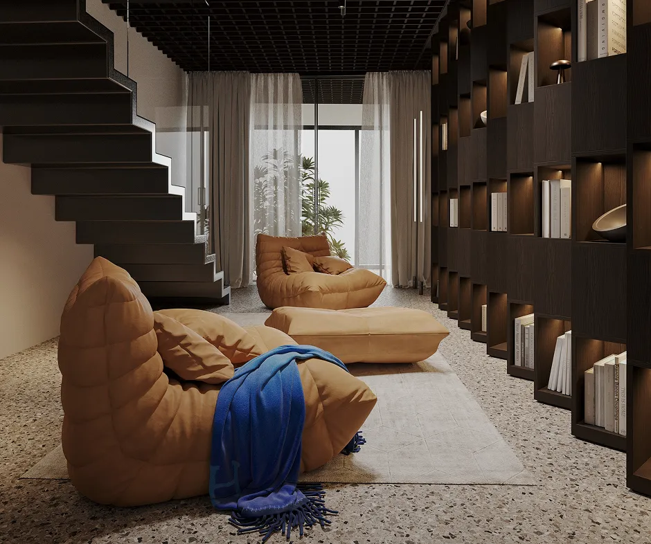 Modern living room with brown cushioned chairs, a matching ottoman, blue throw blanket, terrazzo floor, floating black staircase, sheer curtains, and dark wood wall shelves with books and decor.