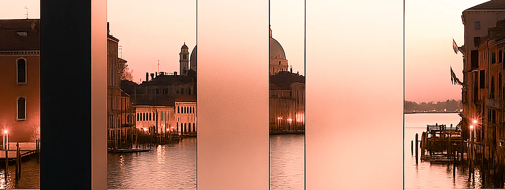 Vista al tramonto di un canale con edifici storici e luci riflesse sull'acqua, vista attraverso lastre verticali sfumate.