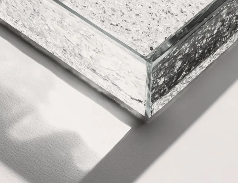 Dettaglio angolare di una lastra di vetro spessa con superficie rugosa o granulata, in ombra su una superficie chiara.