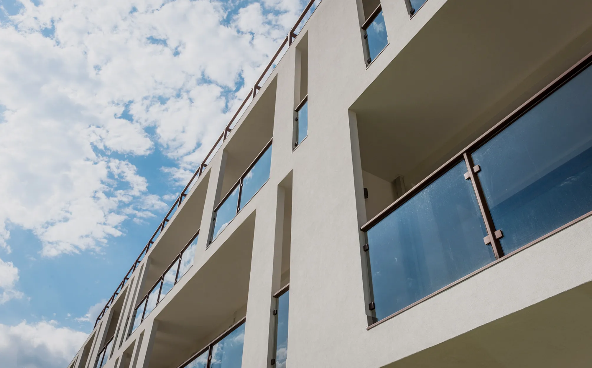 Facciata di un edificio moderno con balconi dotati di parapetti in vetro contro cielo parzialmente nuvoloso.